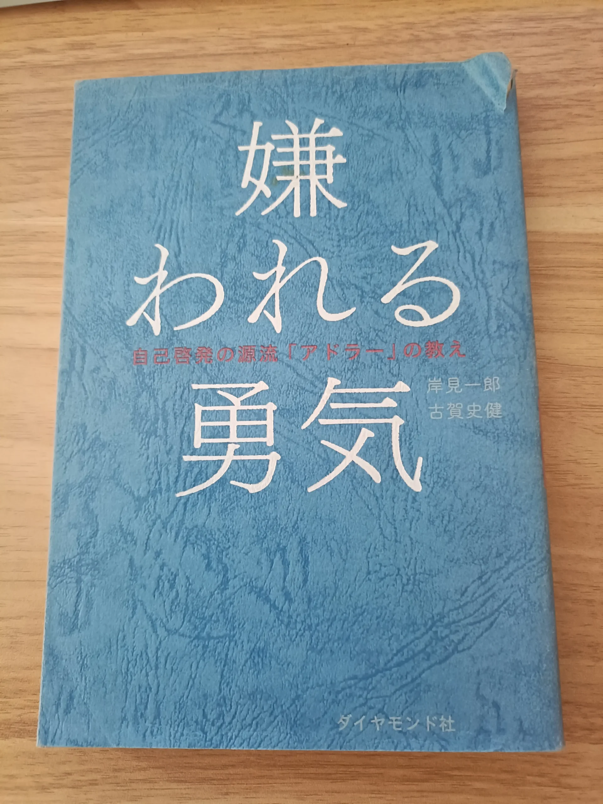 木の机に置いた岸見一郎・古賀史健著『嫌われる勇気』の表紙